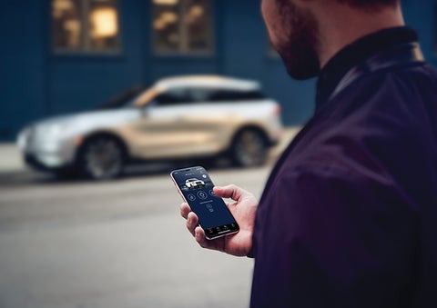 A person is shown interacting with a smartphone to connect to a Lincoln vehicle across the street. | Lincoln Demo 3 in Wooster OH